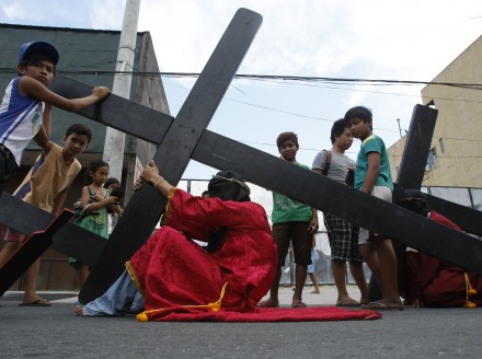 A hooded penitent in the  Philippines pauses while carrying a cross (AP)